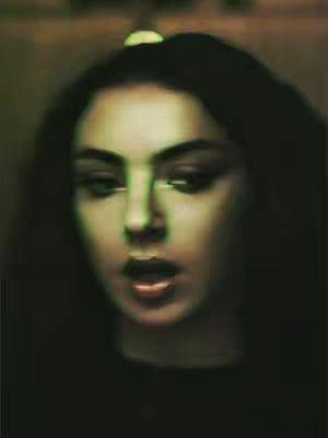 A close-up shot of a young woman with dark hair and a surprised expression. The image has a green and brown color scheme, suggesting the use of a filter or an effect. The woman's mouth is slightly open.