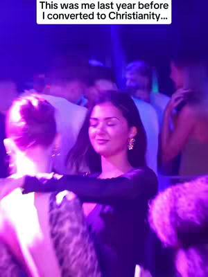 A woman in a black dress dances in a crowded nightclub setting, with disco lights and other partygoers in the background.