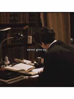 The cover image shows a person in a dark room, likely a study, working at a desk. The person is seen from the back, wearing what appears to be a dark blazer or coat, with dark hair. They are leaning over a desk cluttered with books, papers, and a lamp providing focused light. The image has a warm, slightly desaturated color palette. Text overlayed on the image reads 'never give up'.