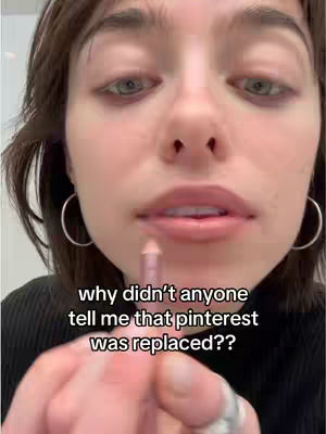 A close-up shot of a person's face with focus on the mouth, holding a lip liner pencil. The individual has short brown hair, hoop earrings, and is looking into the camera. Text overlay on the image asks why no one told them that 'Pinterest was replaced'.