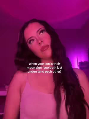 A woman with long dark hair is looking up at the camera with a neutral expression in a room lit with pink light. Text is overlaid on the image.