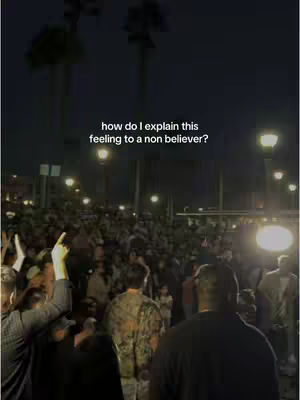 The cover image shows a large crowd of people gathered at night, likely at an outdoor event, with visible streetlights and two tall palm trees in the background. Text overlayed on the image reads, "how do I explain this feeling to a non believer?"