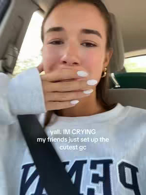 A selfie-style shot of a young woman in a car. The woman has fair skin, long brown hair pulled back, and is wearing a white sweatshirt. She's covering her mouth with her left hand, showing white nail polish. Text overlays at the bottom, appearing to explain what the content is about.