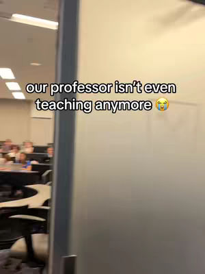The video shows a glimpse inside a classroom with multiple students seated at desks. On the right side of the frame, there is a frosted glass wall and the text overlayed on the image stating, "our professor isn’t even teaching anymore".