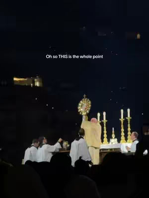 The image shows a nighttime outdoor scene featuring a religious ceremony. In the center, a figure in a robe holds a golden monstrance aloft. Several other people are dressed in white and are positioned around the figure. Behind them are lit candles and what appears to be a church. The sky is dark with a few visible lights, and the overall scene suggests an event of reverence.