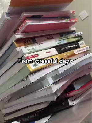 A vertical image showing a messy pile of books, notebooks, and papers stacked on a desk or table, likely in a study environment. There are a variety of colors and the text 'From stressful days' is superimposed on the scene.