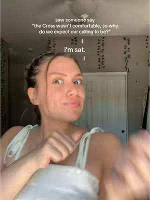 A woman with fair skin stands in a room, looking at the camera with a slightly surprised expression. She has her brown hair pulled back, and is wearing a white top. The background includes a white door, a light fixture, and a wall with patterned detailing. Text overlays are added to the image.