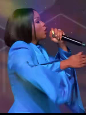 The cover image features a woman on stage holding a microphone, seemingly singing. She is wearing a blue outfit against a blurred background. The image has a vibrant color palette, with dynamic lighting focused on her face and body. The composition is focused on the performer conveying a sense of energy and engagement.