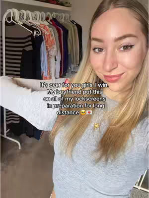 A young woman is shown in a selfie-style shot, standing in a room, likely a bedroom judging from the clothes rack behind her. She's smiling, dressed in a gray shirt, and the lighting seems to be natural. Text overlays are placed on the image to communicate a message.