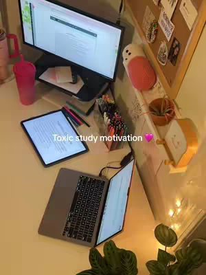 The cover image shows a well-lit workspace with a desk covered in study materials. A laptop is open, displaying a screen. There's a tablet with what seems to be notes, pens, a monitor, a pink tumbler, and a decorative item along with sticky notes on the background. The words 'Toxic study motivation' are overlaid on the image with a heart.