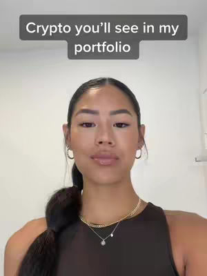 A woman with dark hair in a ponytail is positioned in front of a white background. She wears a black top and jewelry. A text overlay at the top of the image says 'Crypto you'll see in my portfolio'.