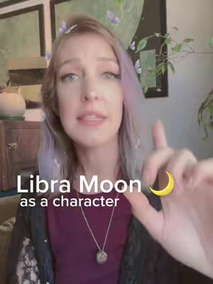 A woman with light purple hair is shown in a selfie-style shot. She is centered, looking at the camera and speaking. The background has a subtle blurred effect with framed artworks and a cabinet on the side. Overlay text indicates the video's topic: Libra Moon as a character, alongside a cartoon crescent moon.