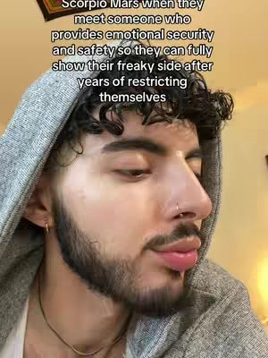 A close-up shot focusing on a light-skinned man with curly dark hair and a light beard. He wears a gray hoodie and a thin gold necklace while looking slightly off-camera. The text overlay depicts the content of the video, and a decorative element is visible on the top left of the frame.