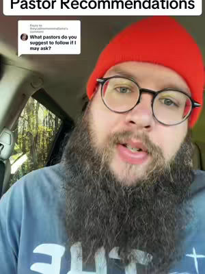A man with a full beard and glasses in a car interior. He is wearing a red beanie and a blue shirt, and is talking to the camera. A comment box and partial window are visible in the background.