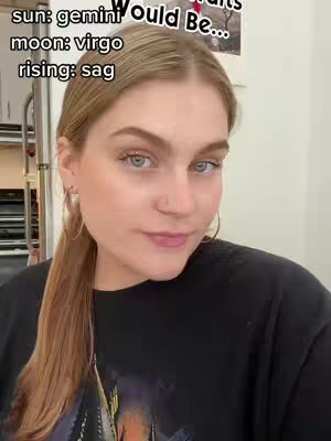 A selfie of a woman with blonde hair pulled back in a low ponytail. She is wearing a black shirt and hoop earrings. Text is overlaid on the image describing the sun, moon, and rising signs.
