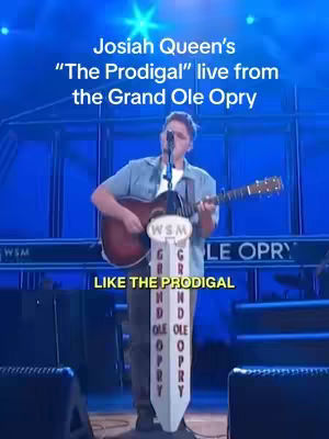 A man singing and playing guitar onstage, the Grand Ole Opry in the background.