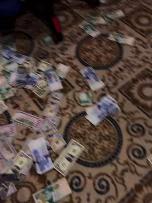 A room with a patterned carpet scattered with various denominations of U.S. dollar bills. The lighting appears natural, and the composition is from a slightly elevated perspective.
