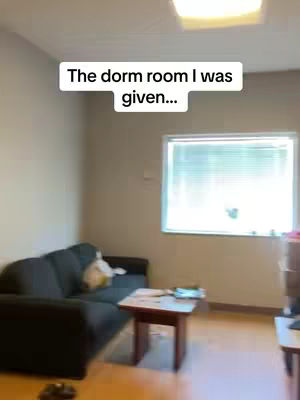 The image shows a room with a couch, a small table, and a window. The text overlay says: The dorm room I was given...