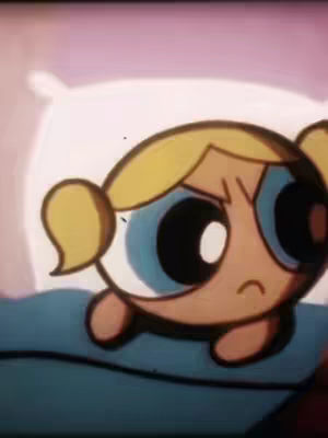 The image features a close-up of Bubbles from The Powerpuff Girls, with a slightly sad or concerned expression. She is nestled in what appears to be a bed, with a blue blanket and a white pillow in the background. Her yellow hair is in pigtails, and she has large blue eyes with a downturned mouth.