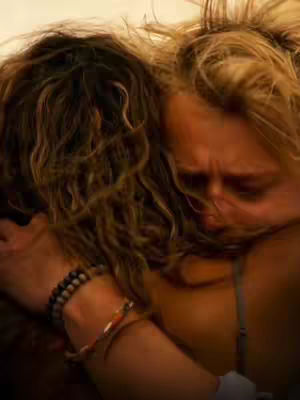 The image captures a close-up of two individuals embracing, their faces pressed close together. The focus is on the intertwined bodies, emphasizing a sense of closeness and intimacy. The surrounding details are blurred, highlighting the emotional connection between the subjects. The lighting is warm and soft, which enhances the intimate atmosphere.