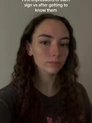 A medium shot featuring a person with long, wavy brown hair, looking directly at the camera with a neutral expression. The background is a solid, light-colored wall. Overlay text appears at the top.