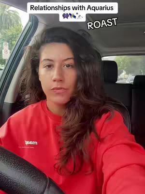 A woman is seated in a car, facing the camera with a neutral expression. She has long, wavy brown hair and is wearing a red sweatshirt. Above her head is a text overlay that says "Relationships with Aquarius" with a small graphic of the Aquarius symbol. The background shows the interior of the car, including the steering wheel and side window, with a glimpse of the outside.