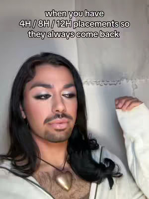 A person with long dark hair and makeup is in front of a white wall. Text is overlayed on top, with the person's face slightly angled to the left, wearing a necklace with a heart-shaped pendant. The text is in white, against a transparent background.
