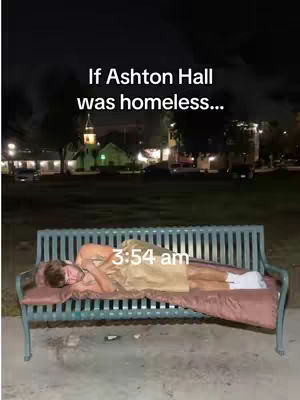A person lies on a park bench at night, covered in a blanket. The scene has a dark background with some lights. The image has a hook text, and indicates an action is happening.
