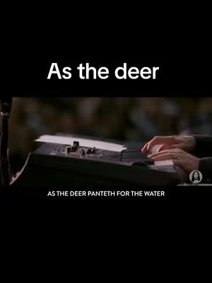 The cover image is a vertical shot with a black background. The top portion displays the text "As the deer" in white, centered. Below, a blurred image shows hands playing a keyboard or piano, suggesting a musician or performer. At the bottom, the text "AS THE DEER PANTEHT FOR THE WATER" is displayed in white. A profile picture is on the bottom right corner.