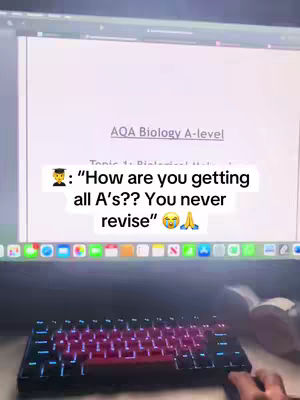 The cover image shows a laptop screen displaying a document, a keyboard, and a portion of a person's hands. The screen shows text, including 'AQA Biology A-level'. Overlayed on the screen is a text bubble containing the text, and a graduation cap emoji. A keyboard with lit keys dominates the bottom. The overall lighting is soft, with a glow emanating from the screen and keyboard.