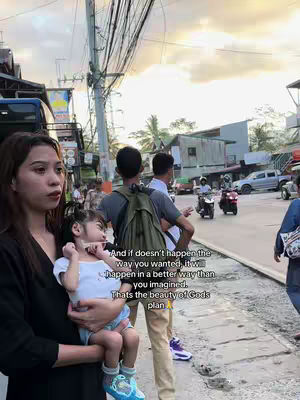 A woman holds a young child in her arms, standing on a city street. A man with a backpack and another man are walking behind them, and there are also other people on the street along with cars and scooters. The text overlay saying: And if doesn't happen the way you wanted, it will happen in a better way than you imagined. Thats the beauty of Gods plan.