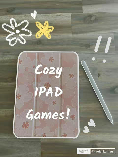 The image shows a wooden surface with an iPad in a patterned case, a stylus, and decorative elements. The iPad is encased in a pink cover with a floral pattern. The text overlay on the iPad says "Cozy IPAD Games!". To the right of the iPad is a silver stylus. Above the iPad are drawn white and yellow flowers. Near the stylus, there are small white heart shapes. The background is a wooden floor.