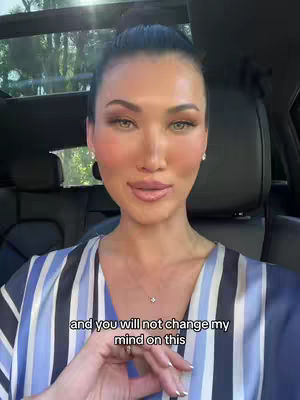 A woman with fair skin and dark hair in a high bun is the central focus. She wears a blue and white striped shirt and a delicate necklace. The background shows the interior of a car, with the sun shining through the window. Text at the bottom of the image reads, 'and you will not change my mind on this.'