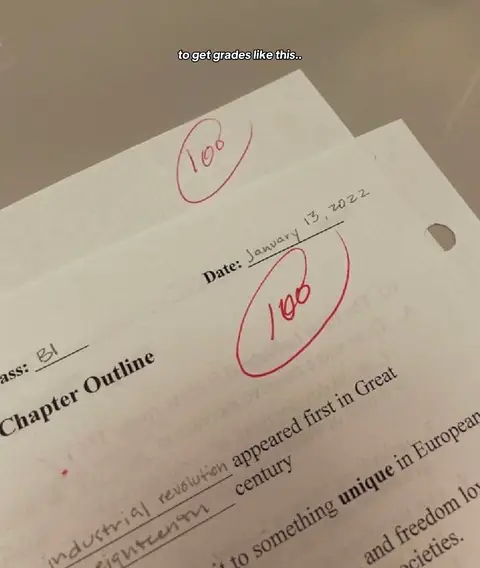 Two sheets of paper with a '100' written in red pen inside a circle, indicating a perfect score. They are slightly askew, showing the date as January 13, 2022.