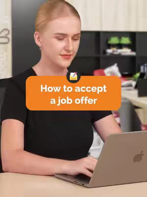 A woman with blonde hair is sitting at a desk in an office. She is looking at a laptop and appears to be typing. A text overlay in a orange box reads: "How to accept a job offer". The background includes office shelves.