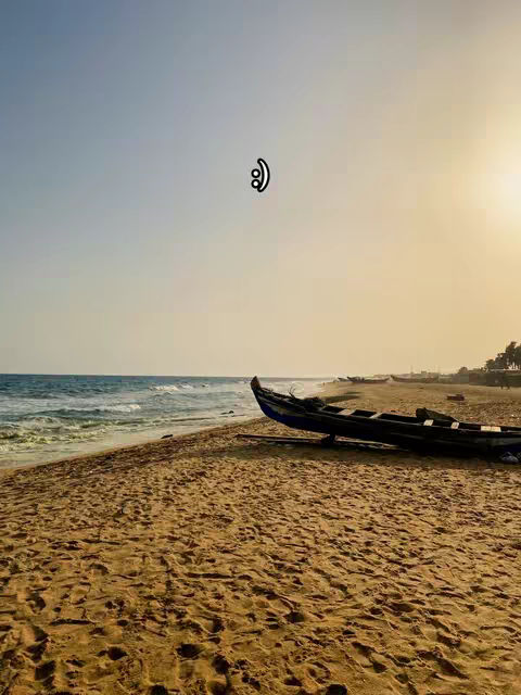A beach scene at sunset with a wooden boat washed ashore. The sky is a gradient of blues and yellows, and the sand is a warm tan color. The boat is dark, and positioned  on the right side.