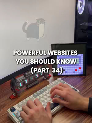 The image shows a desk setting. A person's hands are visible typing on a white mechanical keyboard. To the left is a digital clock with glowing green numbers and a small screen, beyond which is a black monitor showing a game. Behind it is a white wall with a cartoon cat sticker. The hook text 'POWERFUL WEBSITES YOU SHOULD KNOW (PART 34)' is overlayed on the top. The overall composition is clean and focused on the workspace.