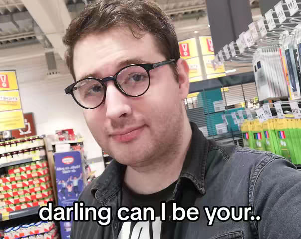 A selfie-style shot taken inside what appears to be a store, with the focus on a man wearing glasses. The background is a bit blurred, but shelves and products are visible. The lighting seems natural, and the man is looking directly at the camera.