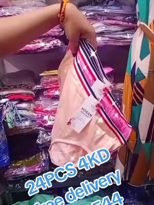 A hand holds up a stack of light pink women's underwear, with a price tag visible. The background shows shelves of folded clothing items, suggesting a store setting. The image is lit with overhead lighting.