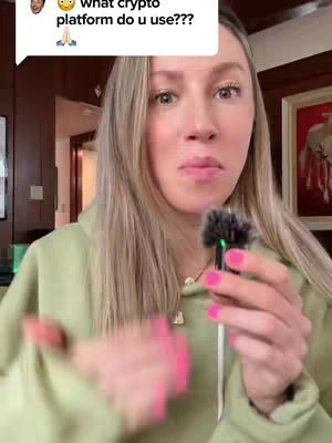 A woman with long blonde hair is holding a small microphone, looking towards the camera. She is wearing a light green hoodie, and her nails are painted pink. The background is a blurred room with wooden panels. A comment bubble in the top left corner features text and a cartoon face.