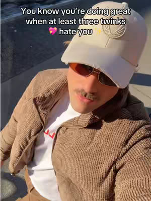 A man wearing sunglasses, a cap and a brown jacket, the man is smiling, the image features text overlay, with a blurred background of a street.