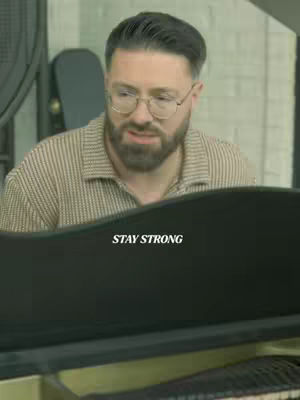 The cover image features a man with glasses and a beard, sitting at a piano. The text overlay reads "STAY STRONG". The background appears to be a room with a window or a large opening.
