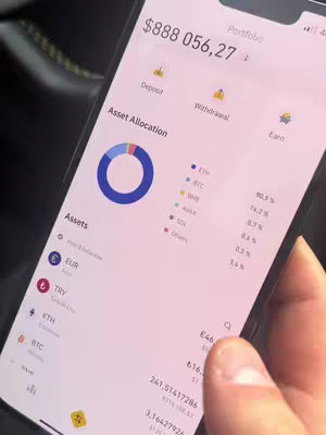 A close-up shot of a smartphone screen displaying a cryptocurrency portfolio. The screen shows a pie chart representing asset allocation, alongside detailed information on various cryptocurrencies like ETH, BTC, and others, including their current values and percentages. The screen is held by a hand, suggesting the user is interacting with the app. In the background, a dark interior hints at the setting.
