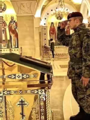 A man in a military uniform salutes inside a church. The interior has ornate decorations, including religious icons and gold accents. The lighting suggests a formal, possibly solemn event.