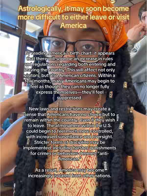 A selfie-style shot. A dark-skinned person with braids and glasses is in the center, wearing an orange headscarf and a patterned top. Text overlays the image, with text in the background. The background is slightly blurred, suggesting an indoor setting.
