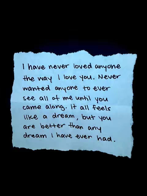 A close-up shot showcasing a light blue, torn piece of paper against a black background. Handwritten on the paper are the words of a romantic quote, with black ink forming the text. The paper is roughly rectangular with uneven edges, adding a handcrafted feel. The contrast between the paper and the dark backdrop makes the text stand out prominently.