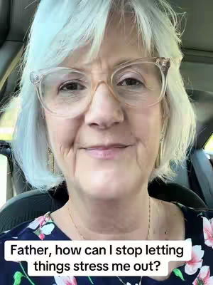A woman with short, light-colored hair and glasses is centered in a selfie-style shot. She is looking directly at the camera with a slight smile. The background appears to be the interior of a car.