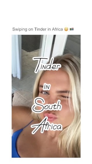 A selfie of a woman with blonde hair, winking and puckering her lips. Text overlay displays the words "Tinder IN South Africa" in a handwritten style, with a white outline. Soft lighting, the background is blurred and out of focus.