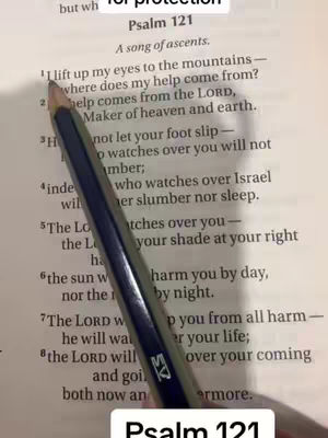 A close-up shot of a page from a Bible with the text of Psalm 121 highlighted. A pencil is pointing at the first verse. The background is slightly blurred, with warm lighting.