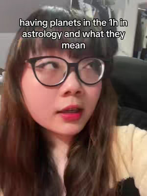 A young woman with black-framed glasses and red lipstick looks slightly off-camera with a questioning expression. The background is blurred, suggesting an interior setting.